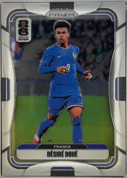Front of 2026 Panini Prizm FIFA DÉSIRÉ DOUÉ #31 Base, portrait-oriented soccer card front. A full-body image of a France player in a blue kit occupies the center against a stadium background. The…