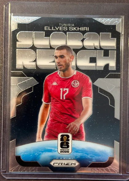 Front of 2026 Panini Prizm FIFA Global Reach Ellyes Skhiri #20 Prizm, portrait soccer card front. The upper section has a black background with large metallic silver PRIZM lettering behind the player. TUNISIA appears…