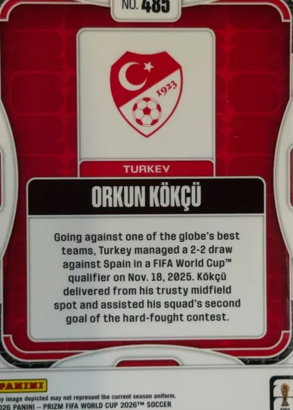 Back of 2026 Panini Prizm FIFA Orkun Kökçü #485 Base Prizm, back of a soccer card in upright orientation. A red patterned background is enclosed by white rounded framing. At the top center is a white label…