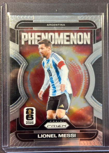 Front of 2026 Panini Prizm FIFA Phenomenon Lionel Messi #19, front-oriented portrait soccer card. ARGENTINA appears in a black top panel, with PHENOMENON in large white lettering below. Lionel Messi is…