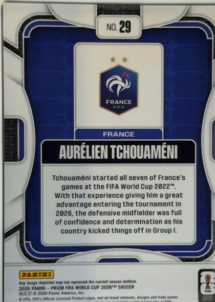 Back of 2026 Panini Prizm FIFA Soccer Cards AURÉLIEN TCHOUAMÉNI #29, portrait-oriented player card back. A dark blue rounded rectangular panel with white and metallic-silver decorative framing fills most of the card…