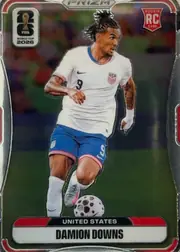 Front of 2026 Panini Prizm FIFA Soccer Cards Damion Downs #436, portrait soccer card front showing Damion Downs in a United States white jersey and blue shorts running with a soccer ball. The player image fills…