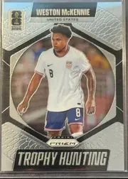 Front of 2026 Panini Prizm FIFA Trophy Hunting Weston McKennie #21, portrait-oriented soccer card front. The player's name appears in large white uppercase lettering on a black banner at the top, with UNITED STATES…