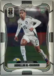 Front of 2026 Panini Prizm FIFA World Cup Soccer ABDULLAH AL-KHAIBARI #586, upright portrait soccer card front. A male soccer player in a white Saudi Arabia uniform with number 15 is shown running with a ball on a dark…