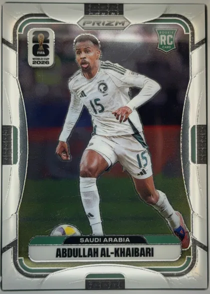 Front of 2026 Panini Prizm FIFA World Cup Soccer ABDULLAH AL-KHAIBARI #586, upright portrait soccer card front. A male soccer player in a white Saudi Arabia uniform with number 15 is shown running with a ball on a dark…