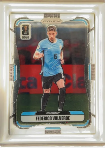 Front of 2026 Panini Prizm FIFA World Cup Soccer Federico Valverde, portrait soccer card front. A player in a light blue Uruguay uniform runs centrally against a stadium background. The PRIZM logo is centered near…