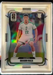 Front of 2026 Panini Prizm FIFA World Cup Soccer Ibrahim Maza, upright portrait soccer card front. A young player in an Algeria white kit numbered 22 is centered over a colorful stadium background. The upper…