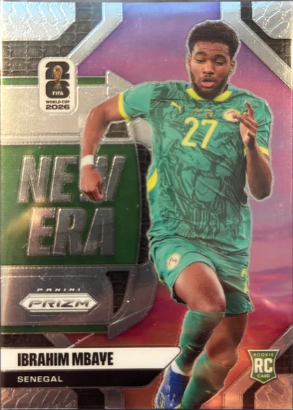 Front of 2026 Panini Prizm FIFA World Cup Soccer Ibrahima Mbaye #26 Rookie Card, portrait-oriented soccer card front. A full-body action image of Ibrahima Mbaye in a green Senegal uniform occupies the right side. The left side…