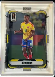Front of 2026 Panini Prizm FIFA World Cup Soccer JHON ARIAS #181, upright portrait soccer card. A full-body photograph of a player in a yellow Colombia jersey occupies the center against a blurred stadium…