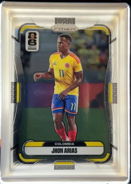 Front of 2026 Panini Prizm FIFA World Cup Soccer JHON ARIAS #181, upright portrait soccer card. A full-body photograph of a player in a yellow Colombia jersey occupies the center against a blurred stadium…