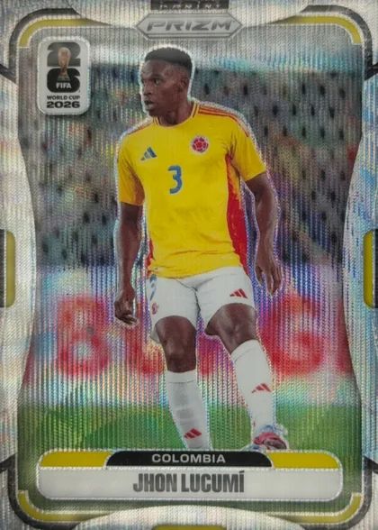 Front of 2026 Panini Prizm FIFA World Cup Soccer Jhon Lucumí, front of a soccer card. Top center has a silver hexagonal 'PRIZM' logo. Top left has a white rounded badge with a large '26', the FIFA World Cup…