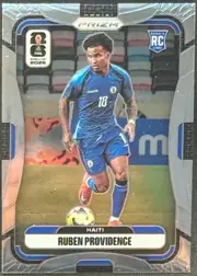 Front of 2026 Panini Prizm FIFA World Cup Soccer Ruben Providence #240 Rookie Card, upright portrait soccer card. A male soccer player in a blue Haiti kit, number 18, is shown running with a ball on a stadium field. The top contains…