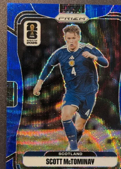 Front of 2026 Panini Prizm FIFA World Cup Soccer Scott McTominay #393 Blue Wave Prizm /55, portrait soccer card front. A large full-body image of Scott McTominay in a blue Scotland uniform occupies the center-right. A FIFA World Cup 2026…
