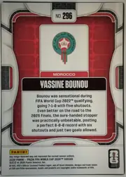 Back of 2026 Panini Prizm FIFA World Cup Soccer Yassine Bounou #296, upright portrait-oriented card back. A silver-white and black patterned outer frame surrounds a red inset panel with rounded corners and thin white…