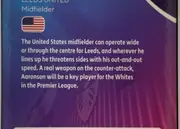 Back of Topps Chrome Brenden Aaronson Base, back side of a football card dominated by a blue-to-purple gradient with vertical tonal stripes and a faint football-themed graphic. At the upper…