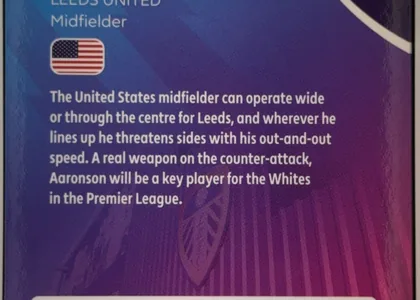 Back of Topps Chrome Brenden Aaronson Base, back side of a football card dominated by a blue-to-purple gradient with vertical tonal stripes and a faint football-themed graphic. At the upper…